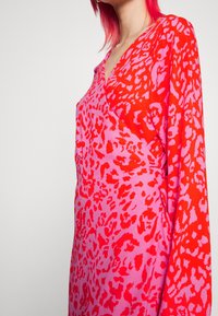 Rotes und pinkes Tierdruckkleid mit V-Ausschnitt und langen Ärmeln. Der Stoff hat eine glatte Textur und auffällige, kontrastierende Muster.