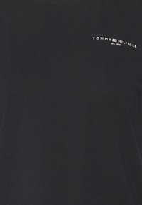 Černé bavlněné tričko s kulatým výstřihem. Obsahuje bílé logo, které zní "TOMMY HILFIGER EST. 1985" na levé horní části hrudi.