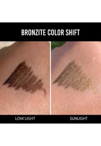 Campione di cambio colore della bronzite sulla pelle, che mostra un marrone scuro in scarsa illuminazione e una tonalità bronzo più chiara alla luce del sole. Differenze di texture chiaramente visibili.