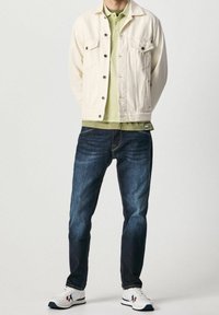 Bílá džínová bunda, světle zelené polo, tmavě modré džíny a bílé tenisky s červenými a modrými akcenty. Ležérní střih a čisté linie.