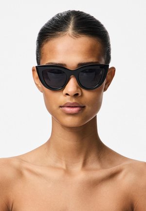Zwarte cat-eye zonnebril met donkere lenzen. Dikke, gladde kunststof frame. Hoekig ontwerp benadrukt scherpe randen en eigentijdse stijl.