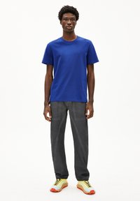 Blaues Baumwoll-T-Shirt mit kurzen Ärmeln, kombiniert mit dunkelgrauen Hosen und mehrfarbigen Sneakern mit gelben, hellblauen und roten Akzenten.
