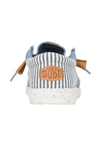 Scarpa slip-on a righe blu e bianche con un'emblema in pelle marrone. Caratterizzata da una forma arrotondata, una tomaia in tessuto morbido e una suola bianca maculata.