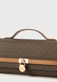 Tumepruun mustriga käekott, millel on helepruun nahast ääris, ülemine käepide ja kuldne ümara kujuga luku kinnis, millel on "MK" logo.