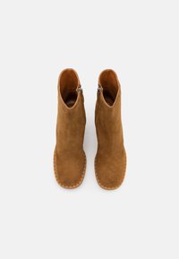 Tan suede ankle boots with a smooth texture, rounded toes, and side zippers. Features a light rubber outsole with a ridged pattern.
