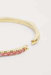 Le bracelet en ton or présente un design courbé avec des pierres précieuses roses serties de griffes le long du centre. Mécanisme de fermoir visible à une extrémité.