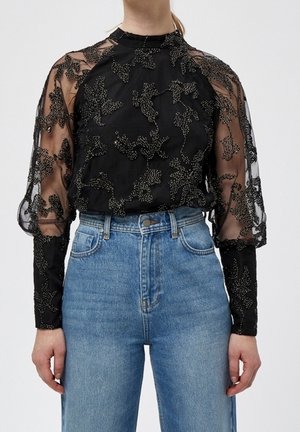 Schwarze transparente Bluse mit floraler Perlenstickerei, getragen zu hoch taillierten blauen Jeans, mit detaillierten langen Ärmeln und hohem Kragen.
