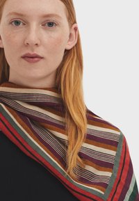 Multicolored striped scarf featuring bold horizontal lines in shades of red, green, purple, and cream, made of a soft fabric.