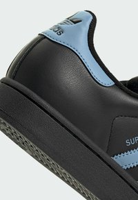 Black leather sneaker with light blue accents, textured sole, and embossed logo. Rounded toe and cushioned collar for support.