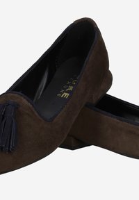 Mocassins en cuir suédé marron avec un talon plat, dotés d'un liseré bleu marine et d'un gland décoratif à l'avant. Finition intérieure lisse.