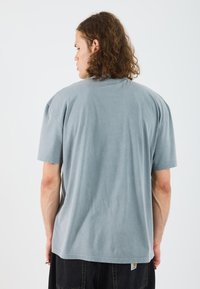 Camiseta de manga corta azul claro. Tejido suave, corte relajado, escote redondo. Dobladillo recto con etiqueta en el lado inferior. Diseño minimalista.