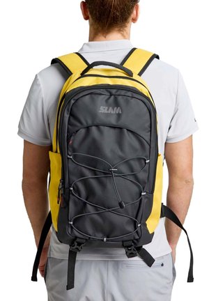 Una persona vista desde atrás lleva una mochila negra y amarilla con un cordón elástico en la parte delantera y varios compartimentos con cremallera.