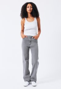 Lichtgrijze geribde tanktop gecombineerd met lichtgrijze rechte jeans. De jeans hebben een klassiek vijf-pocketontwerp en subtiele stikdetails.