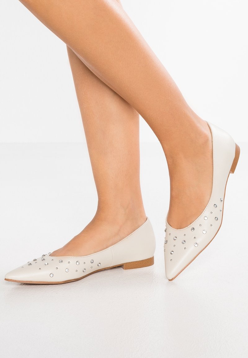 Chaussures plates beige pâle avec un bout pointu et un petit talon, ornées de strass clairs sur la surface supérieure.