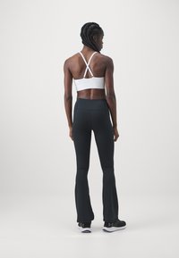 White sports bra with cross-back straps and black high-waisted flared leggings. Both garments have a smooth texture and a fitted design.