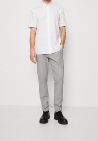 Bílé košile s krátkým rukávem a knoflíky, světle šedé kalhoty na míru a černé platformové boty. Výrazný límec a hladké textury látky.