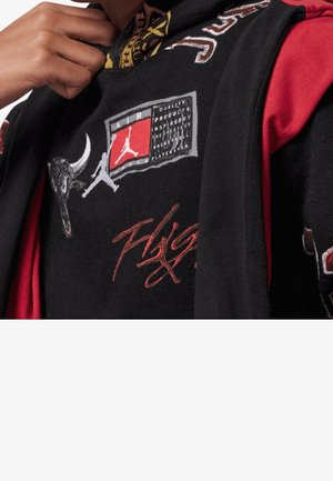 Personne portant des vêtements superposés rouges et noirs arborant les logos Air Jordan et Chicago Bulls, avec un poing levé près du cou.