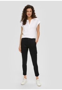 Witte linnen top met korte mouwen en een V-hals, gecombineerd met zwarte cargobroek met zijzakken en witte sneakers.