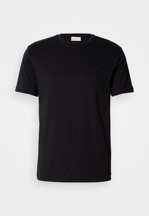 Camiseta de algodón negra con cuello redondo y mangas cortas, que presenta un logotipo bordado tono sobre tono en el lado izquierdo del pecho. Textura suave.