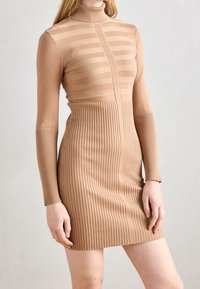 Robe tricotée d'une douce couleur beige, dotée d'un col montant, d'un motif rayé sur le buste et d'une texture côtelée sur la moitié inférieure.