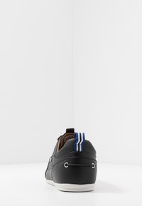 Black leather sneakers with a smooth finish, white sole, and blue-striped heel tab. Features decorative eyelets on the sides.