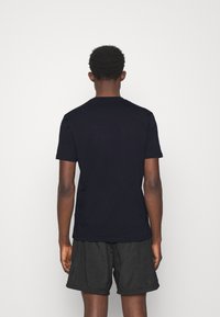 Schwarzes kurzärmeliges T-Shirt aus Baumwolle; Rundhalsausschnitt-Design mit glatter Textur; getragen mit dunkelgefärbten Shorts, von hinten betrachtet.