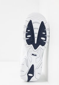 Semelle blanche de basket avec motifs d’adhérence noirs, rainures courbées et logo FILA centré sur la bande de roulement inférieure.