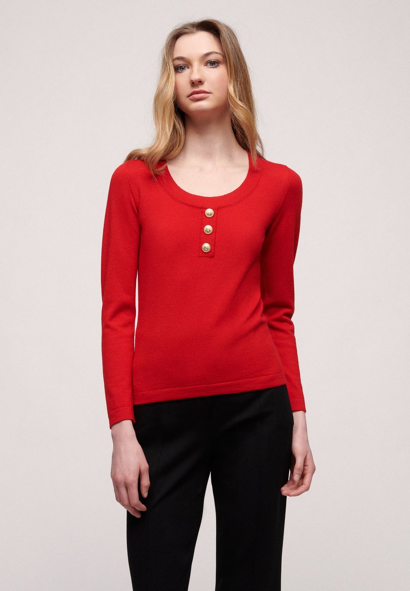 Red long-sleeve sweater with a scoop neckline, featuring four gold-tone buttons down the front. Soft fabric and fitted design.
