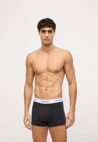 Czarne bokserki z geometrycznym wzorem, biała elastyczna talia z logo Calvin Klein, materiał bawełniany, dopasowany krój.