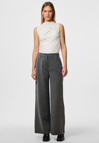 Pantaloni grigi a gamba larga con una finitura testurizzata, dotati di chiusura frontale con bottone e due tasche laterali, abbinati a un top aderente color crema.