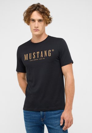 Schwarzes Baumwoll-T-Shirt mit kurzen Ärmeln, das "MUSTANG" in fetter, goldener Schrift zeigt. Lässiger Schnitt, minimalistisches Design, glatte Textur.