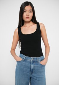 Čierny rebrovaný top s okrúhlym výstrihom, skombinovaný s bledomodrými džínsami s vysokým pásom; model má ruky vo vreckách.