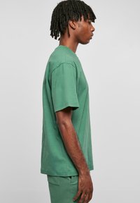 Tricou verde din bumbac, cu mâneci scurte, guler rotund și o croială lejeră. Țesătura are o textură netedă și este combinată cu pantaloni asortați.