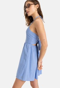 Blue cotton dress with a halter neck, cut-out sides, and a tied back. Features a textured fabric and a flared skirt.