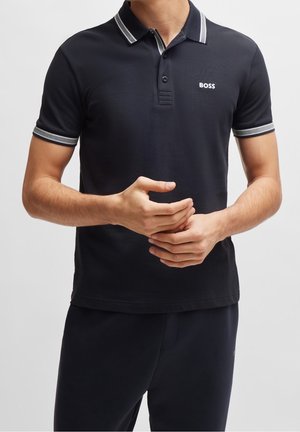 Zwarte poloshirt van een gestructureerde stof, met contrasterende gestreepte kraag en mouwen, en een klein wit logo op de borst.