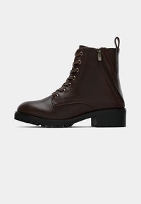 Brązowy skórzany but za kostkę z okrągłym noskiem, sznurowanym przodem, bocznym zamkiem błyskawicznym i wytrzymałą czarną podeszwą. Gładka tekstura z minimalnym zdobieniem.