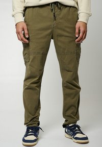 Pantalones cargo verde olivo con múltiples bolsillos, cintura elástica y cordón. Presentan un corte relajado y sutiles detalles desgastados.