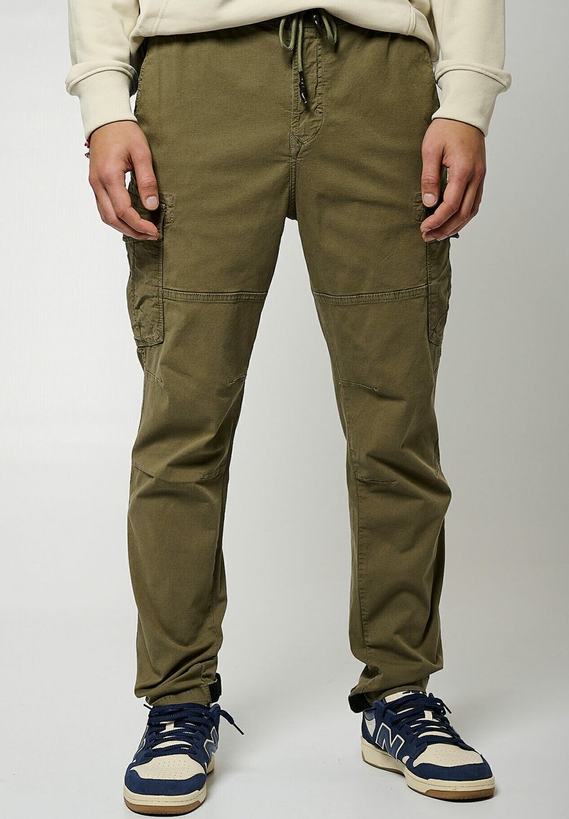 Pantalones cargo verde olivo con múltiples bolsillos, cintura elástica y cordón. Presentan un corte relajado y sutiles detalles desgastados.