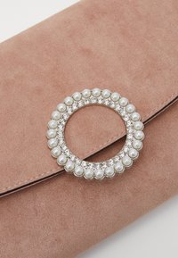 Jasnoróżowa zamszowa kopertówka z okrągłą klamrą ozdobioną perłami i przezroczystymi cyrkoniami na przedniej klapie.