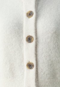 Cream-colored cardigan made of soft knit material, featuring four round buttons with a marbled finish and ribbed edge detailing.