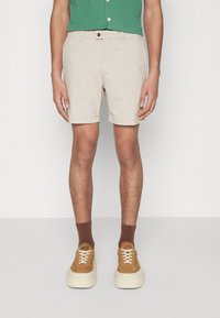 Beiga shorts i lättviktig tyg med knappstängning fram, sidofickor och en avslappnad passform. Kombinerat med bruna ankelsockor och beiga sneakers.