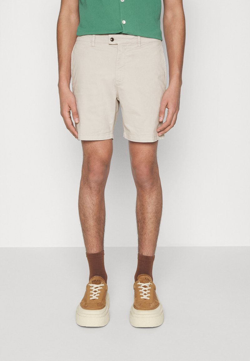 Beiga shorts i lättviktig tyg med knappstängning fram, sidofickor och en avslappnad passform. Kombinerat med bruna ankelsockor och beiga sneakers.