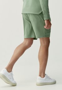 Gröna shorts i lätt material med en slät textur, utrustade med sidofickor och en figurnära stil, tillsammans med vita sneakers.
