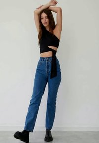 Black one-shoulder crop top with a side tie, paired with high-waisted blue denim jeans and black ankle boots. Simple, fitted design.