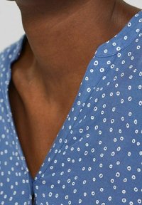 Top blu con scollatura a V, realizzato in tessuto leggero con un motivo a pois bianchi.