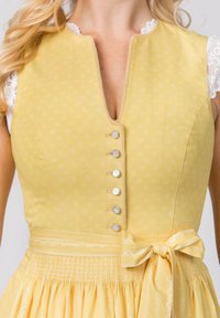 Gelbes Kleid mit tailliertem Oberteil, V-Ausschnitt, Spitzenbesatz und silbernen Knöpfen. Verfügt über einen plissierten Rock mit gebundenem Gürtel und subtilen Blumenmuster.