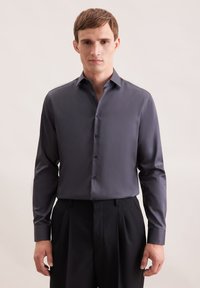 Donkergrijze herenoverhemden met lange mouwen van gladde stof, met een puntige kraag en knoopsluiting. Gepaard met zwarte geplooide broek.