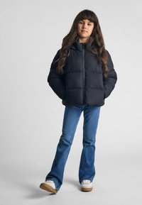 Svart puffjacka med huva, med dragkedjestängning. Kombinerad med utsvängda blå denimjeans och vita sneakers med bruna sulor.