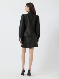 Black tailored jacket with puffed sleeves and a textured pattern, paired with a matching skirt. Features gold button accents.