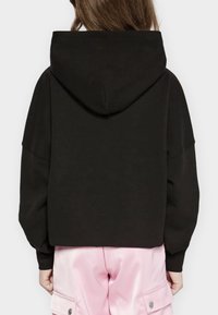 Cropped hoodie nera con un ampio cappuccio, vestibilità comoda e spalle cadenti, abbinata a pantaloni cargo in satin rosa con tasche laterali.